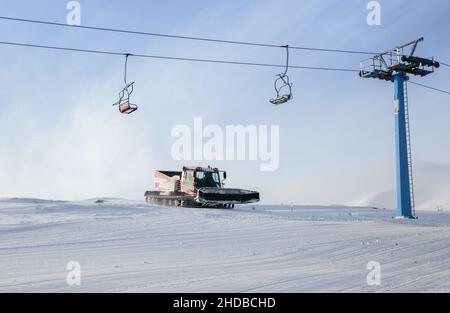 pista da sci curata di neve appena preparata. veicoli cingolati, snowcat e cavi di sollevamento. Stagione invernale, stazione sciistica, freddo tempo di neve soleggiato Foto Stock