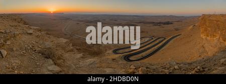 Vista panoramica all'alba di una strada tortuosa e del paesaggio di Makhtesh (cratere) Ramon, nel deserto di Negev, Israele meridionale. È un landfo geologico Foto Stock