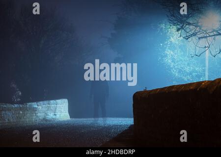 Un concetto horror di una figura fantasma trasparente con cappuccio. In piedi su una strada di campagna in una notte di inverni spooky Foto Stock