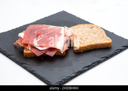 panino integrale con prosciutto crudo e insalata su sfondo bianco Foto Stock