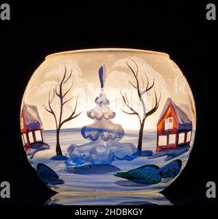 Una tazza di vetro dipinta a mano con paesaggio invernale illuminato da una candela all'interno della tazza. Un primo piano di fotographyand utilizzando la pittura leggera. Foto Stock