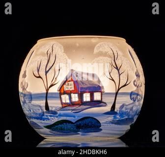 Una tazza di vetro dipinta a mano con paesaggio invernale illuminato da una candela all'interno della tazza. Un primo piano di fotographyand utilizzando la pittura leggera. Foto Stock