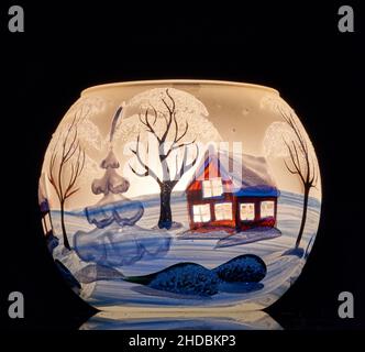 Una tazza di vetro dipinta a mano con paesaggio invernale illuminato da una candela all'interno della tazza. Un primo piano di fotographyand utilizzando la pittura leggera. Foto Stock