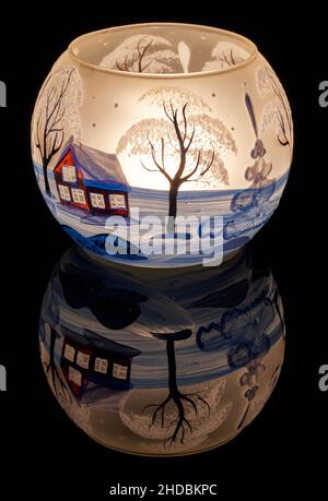 Una tazza di vetro dipinta a mano con paesaggio invernale illuminato da una candela all'interno della tazza. Un primo piano di fotographyand utilizzando la pittura leggera. Foto Stock