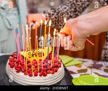 Torta di buon compleanno con candele colorate che bruciano e molte fragole rosse selvatiche Foto Stock