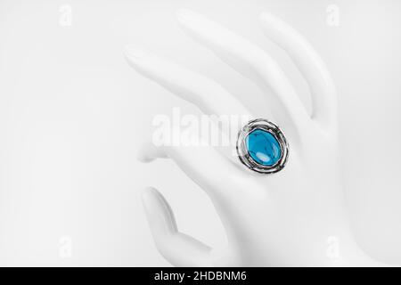 Mano bianca in plastica con anello in argento e pietra turchese su sfondo bianco Foto Stock