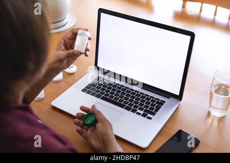 Donna anziana con la medicina che usa il laptop durante la consultazione del medico in linea a casa, spazio di copia Foto Stock
