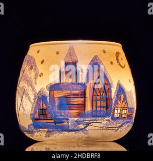 Una tazza di vetro dipinta a mano con paesaggio invernale illuminato da una candela all'interno della tazza. Un primo piano di fotographyand utilizzando la pittura leggera. Foto Stock