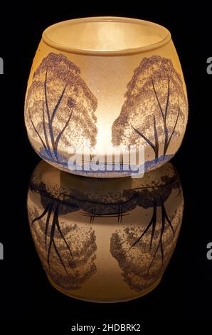 Una tazza di vetro dipinta a mano con paesaggio invernale illuminato da una candela all'interno della tazza. Un primo piano di fotographyand utilizzando la pittura leggera. Foto Stock