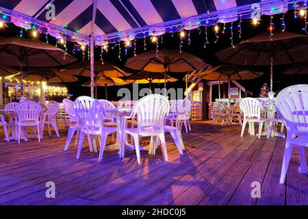 Dopo l'orario di lavoro, terrazza all'aperto vuota e patio con sedie e tavoli in plastica sotto un tarp e ombrelloni di notte con luci di Natale. Foto Stock