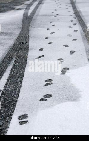 Tracce di pneumatici auto e impronte su sottile manto nevoso di strada asfaltata Foto Stock