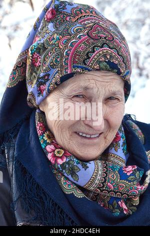 Ritratto di una donna russa anziana con una bella e colorata testa-sciarpa Pavlo Posad su sfondo sfocato inverno. Foto Stock