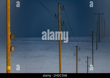 Piloni elettrici in paesaggio invernale contro il cielo drammatico, Oberguenzburg, Ostallgaeu, Baviera, Germania Foto Stock