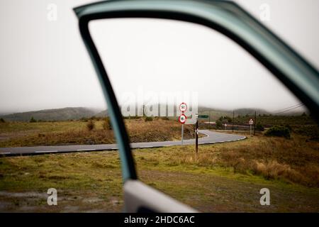 Vista attraverso un finestrino di una strada con segnali di direzione e di limite di velocità in caso di nebbia Foto Stock