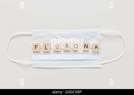 Parola FLURONA su maschera medica, sfondo bianco. COVID e influenza doppia infezione. Prima combinazione di due virus, concetto di coinfezioni respiratorie. Vista dall'alto, spazio di copia Foto Stock