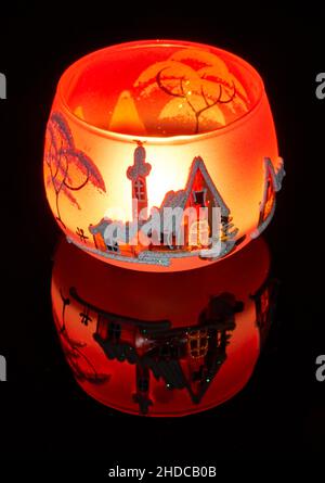 Una tazza di vetro dipinta a mano con paesaggio invernale illuminato da una candela all'interno della tazza. Un primo piano di fotographyand utilizzando la pittura leggera. Foto Stock