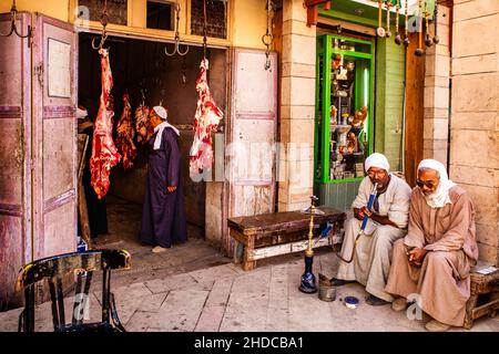 Uomini che fumano pipe d'acqua di fronte ad un macellaio, bazar nella Città Vecchia, Luxor, Tebe, Egitto, Luxor, Tebe, Egitto, Africa Foto Stock