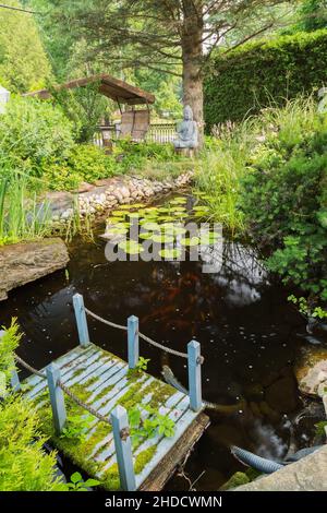 Laghetto con ponte galleggiante in legno dipinto di blu, Iris pseudacoro - Bandiera gialla, Baptizia 'Grape Taffy' - False Indigo, Wild Indigo. Foto Stock