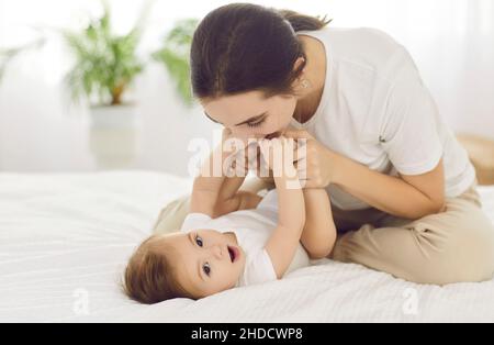 Felice, madre giovane amorevole che tiene le mani del suo bambino e bacia i suoi piedi piccoli Foto Stock