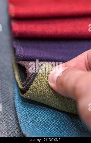 Esempi di tessuti per tappezzeria in diversi colori e spessori. Dettagli closeup dei campioni di tessuto multicolore. Un uomo prende un esempio di Foto Stock