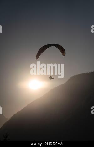 Parapendio sopra la silhouette di un boscosa crinale di montagna con il sole retroilluminato al tramonto Foto Stock