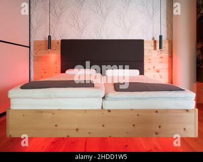 letto in legno di pino con schienale in pelle e due luci appese di fronte alla parete della carta da parati Foto Stock