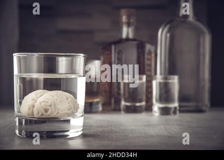 Modello cerebrale umano in un bicchiere con bevanda alcolica, sullo sfondo di bottiglie con alcol. Dipendenza da alcol. Danno da alcol al cervello. Foto Stock