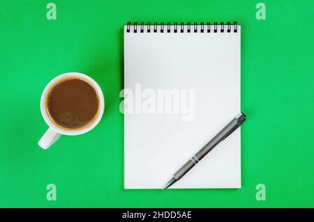 Blocco note con pagine bianche, penna e tazza di caffè su sfondo verde chiaro. Foto Stock