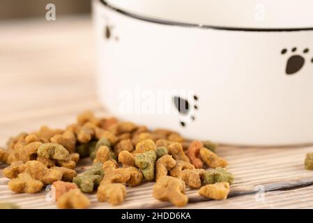 Il cibo secco del cane o del gatto è fuoriuscito dalla ciotola sul pavimento di legno. Foto Stock