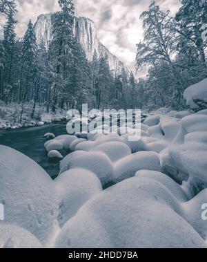 La neve coperte le rocce e la vegetazione lungo il fiume Merced, con il picco El Capitan sullo sfondo, Yosemite National Park, California, USA. Foto Stock