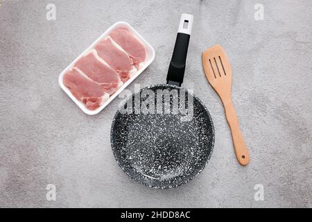 Padella in marmo nero con carne cruda e spatola in legno su sfondo grigio del tavolo, vista dall'alto Foto Stock