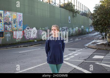 Amy Rafferty di Trademark, Community Organisation fuori dal suo ufficio con dipinti e murales colorati sul muro della Pace, o Peace Line, che corre lungo la Coppa Foto Stock