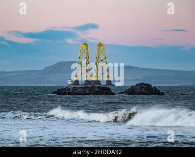 Al tramonto, Firth of Forth, Scozia, Regno Unito, una chiatta che trasporta due enormi turbine eoliche gialle si dirige verso il Mare del Nord Foto Stock