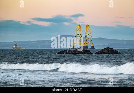 Al tramonto, Firth of Forth, Scozia, Regno Unito, una chiatta che trasporta due enormi turbine eoliche gialle si dirige verso il Mare del Nord Foto Stock