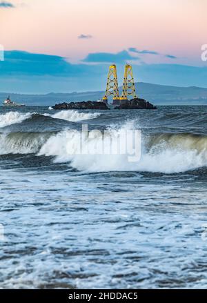 Al tramonto, Firth of Forth, Scozia, Regno Unito, una chiatta che trasporta due enormi turbine eoliche gialle si dirige verso il Mare del Nord Foto Stock