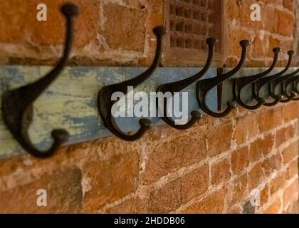 Ferro battuto cappotto appende posto su vecchio legno vintage appeso su una parete testurizzata di mattone con un leftside bianco per lo spazio di copia girato in fuoco selettivo con un Foto Stock