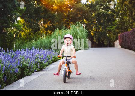 La bambina corre in runbike nel parco estivo. I bambini indossano le imbottiture di protezione e il casco di sicurezza per una guida sicura. Sport all'aperto per bambini. Estate spa Foto Stock