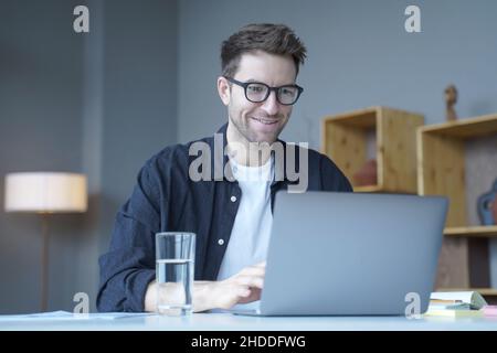 Giovane uomo d'affari sorridente consulente finanziario europeo che lavora in remoto online da casa Foto Stock