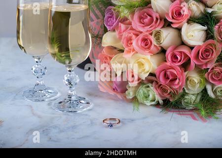 Un bel bouquet nuziale di delicati rose, un anello con diamante, due bicchieri di champagne su un tavolo di marmo. Giorno di festa, wedding. Il giorno di San Valentino Foto Stock
