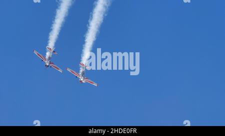 Thiene Italy OTTOBRE, 16, 2021 due velivoli ad elica fanno un giro con fumo bianco nel cielo blu con spazio di copia. Yakovlev Yak-52 di YAK Italia Foto Stock