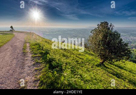 Una figura umana lontana, in piedi, guardando in stupore lo spettacolo del sole estivo che sorge sul paesaggio del Worcestershire, visto dalla cima di NOR Foto Stock