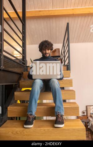 Uomo a basso angolo seduto sui gradini che lavora sul laptop Foto Stock