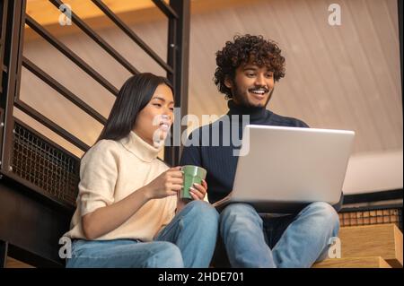 Donna con tazza e uomo che guarda il notebook Foto Stock