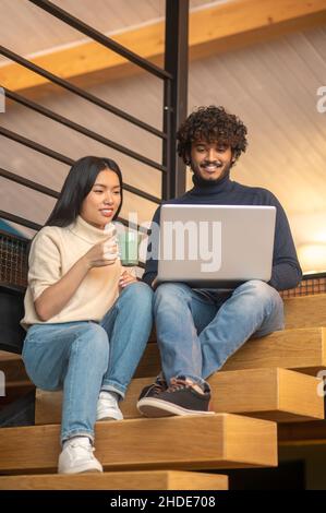 Uomo e donna che guardano un computer portatile seduto sulle scale Foto Stock