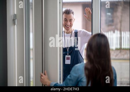 Donna che apre la porta all'uomo con la mano sollevata nel saluto Foto Stock