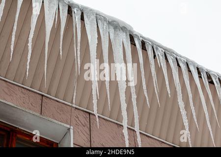 Grandi e lunghe ghiacciate pendono dal tetto dell'edificio. Le ghiacciate creano un pericolo per i pedoni. Foto Stock