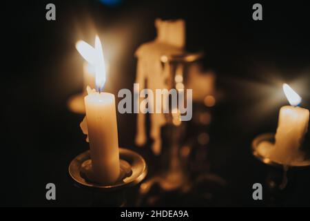 Le candele che bruciano su un vecchio candeliere di ottone su sfondo nero Foto Stock