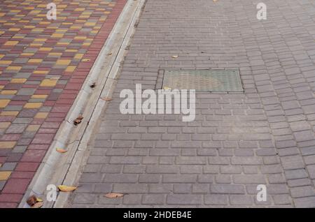 Strada e marciapiede ricoperti di piastrelle colorate. Manhole verde tra le piastrelle grigie. Messa a fuoco selettiva. Foto Stock