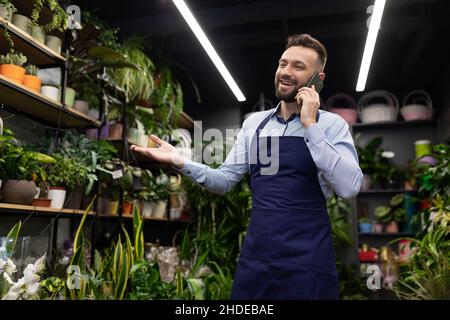 Un fioraio in grembiuli blu in un negozio di fiori e piante in vaso prende un ordine per telefono per San Valentino Foto Stock