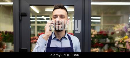 il fiorista in fondo frigorifero con fiori freschi prende un ordine per telefono Foto Stock